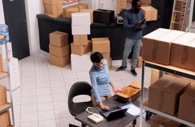 vista-superior-supervisor-almacen-que-empaqueta-pedido-ropa-cliente-caja-carton-mientras-verifica-detalles-envio-computadora-portatil-equipo-trabajando-almacen-departamento-entrega_482257-66036